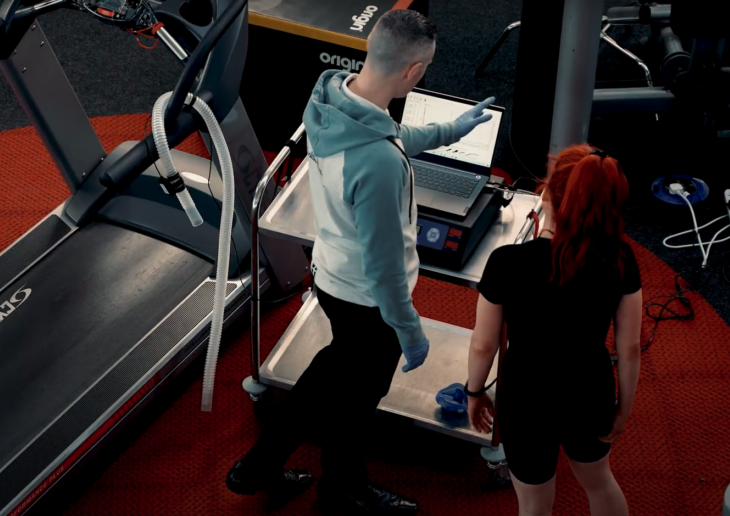 Man showing a woman VO2 graphs on a computer screen beside a treadmill